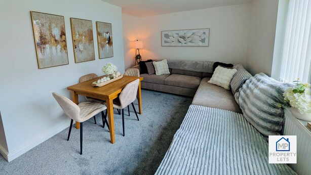 A living room with a wooden dining table, beige chairs, a grey sofa, and a large white flower arrangement. - Stylish Stay Near Gateacre – South Liverpool (Liverpool)
