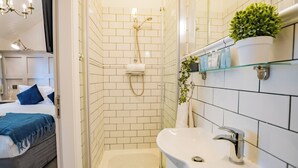 A hotel bathroom with a glass shower enclosure, a white sink, and a mirror with a potted plant. - Modern Studio by Howth Marina (Howth)