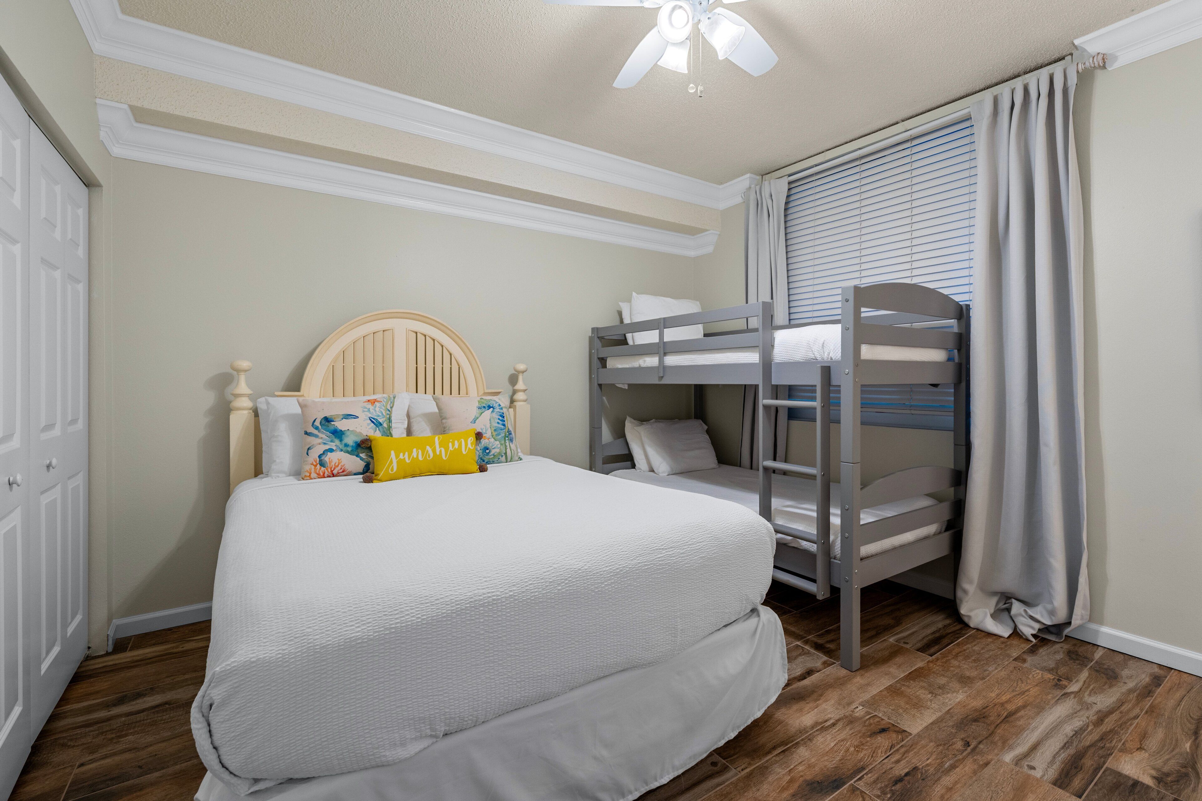 A bedroom with a bunk bed, a single bed, a ceiling fan, and a window with curtains.
