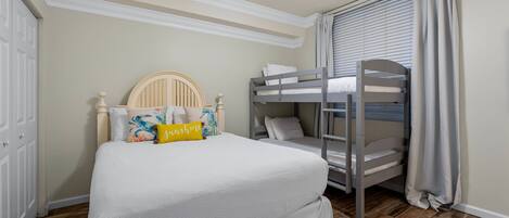 A bedroom with a bunk bed, a single bed, a ceiling fan, and a window with curtains.
