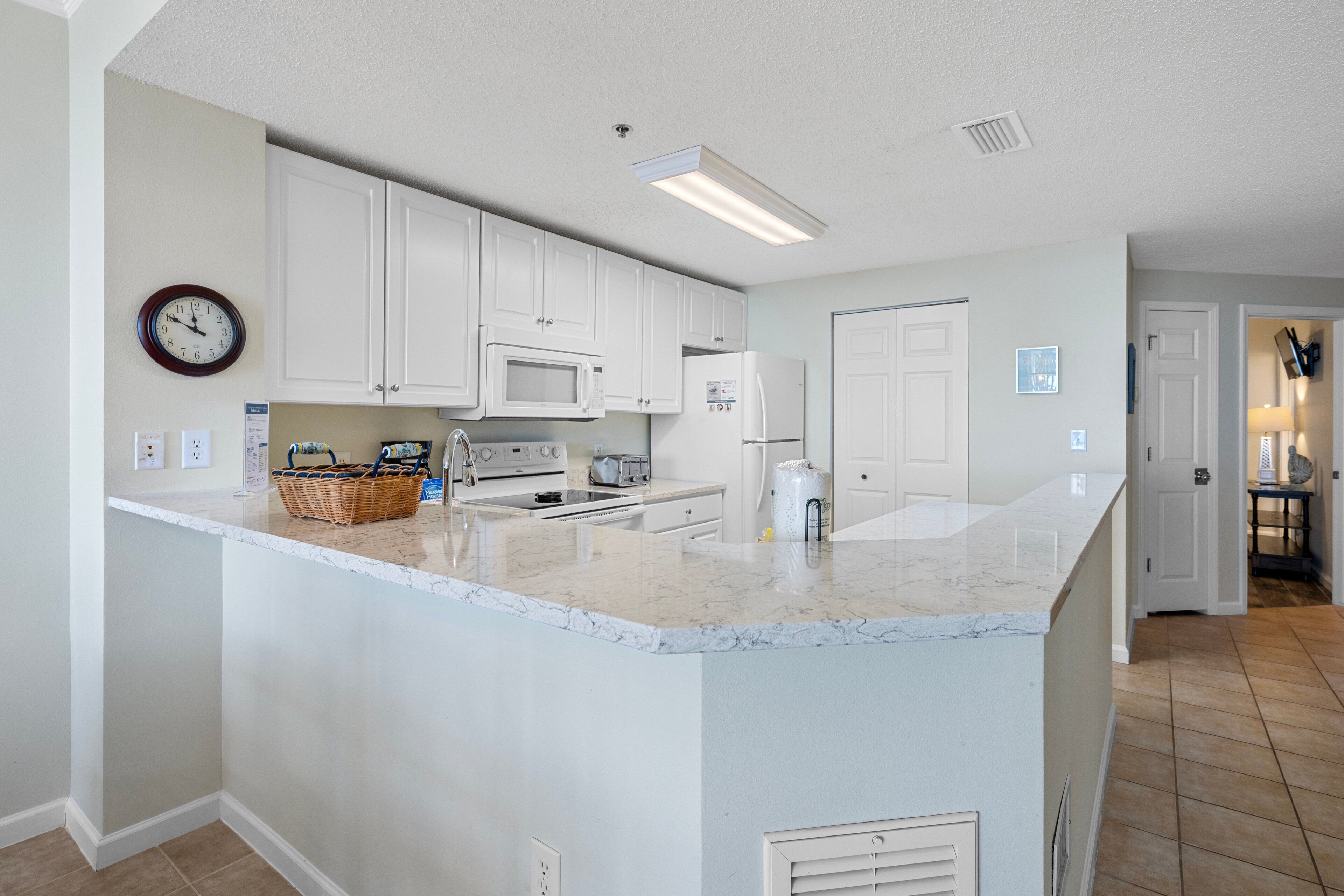 A kitchen with white cabinets, a microwave, a toaster, and a large island with a marble countertop.
