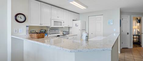 A kitchen with white cabinets, a microwave, a toaster, and a large island with a marble countertop.