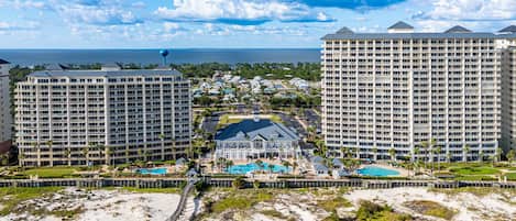 A resort with multiple high-rise buildings, a central pool area, and a beach in the foreground.