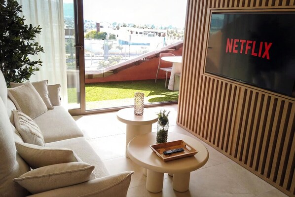 Una sala de estar moderna con un sofá, una mesa de centro y una pantalla de televisión que muestra "NETFLIX".