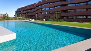 Un edificio moderno con piscina, que presenta una piscina azul cristalina y un césped bien cuidado.
