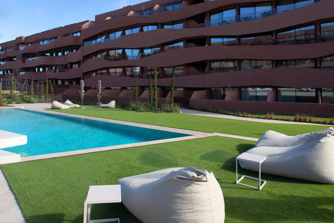 Un edificio moderno con piscina, césped artificial verde y mobiliario de exterior.