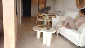 Una sala de estar moderna con un sofá blanco, dos mesitas auxiliares y un comedor con una mesa redonda pequeña y sillas.