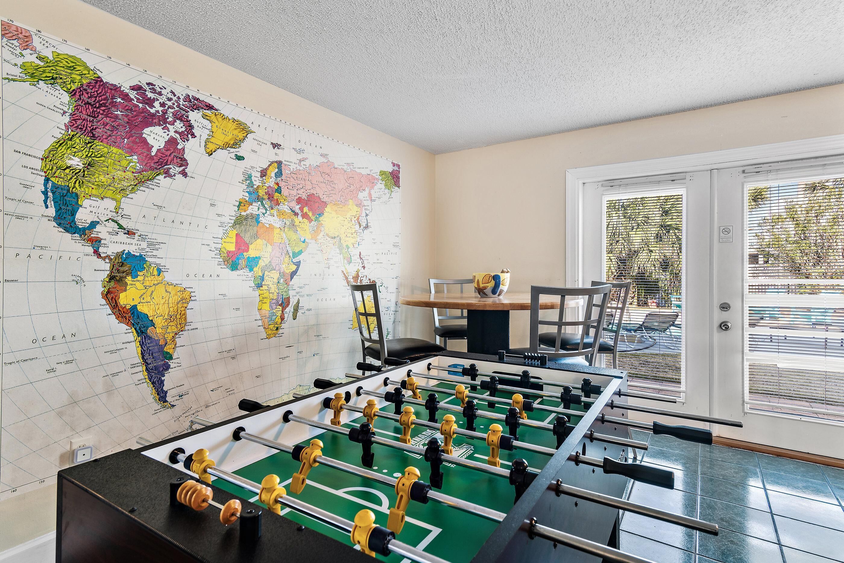 A room with a large world map on the wall, a foosball table, and a dining table with chairs.