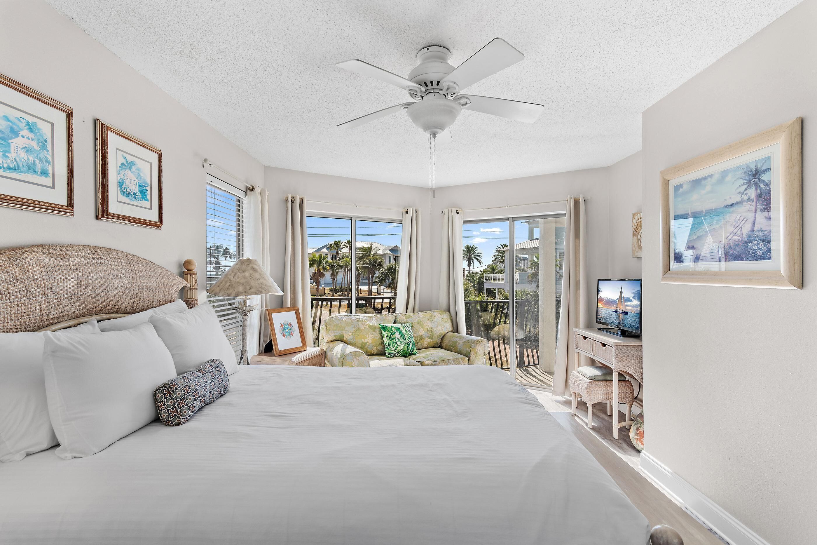 A bedroom with a large bed, a ceiling fan, and a TV on a desk.