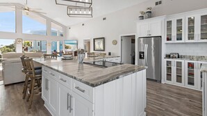 Una cocina amplia con una isla grande, armarios blancos y un refrigerador de acero inoxidable.
