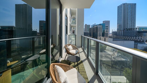 Ein Balkon mit Korbmöbeln, Glasgeländer und Blick auf die Stadt.
