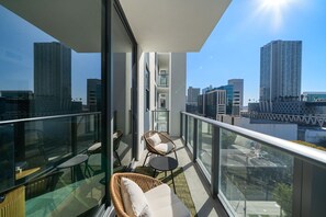 Varanda com móveis de vime, guarda-corpo de vidro e vista para a cidade.