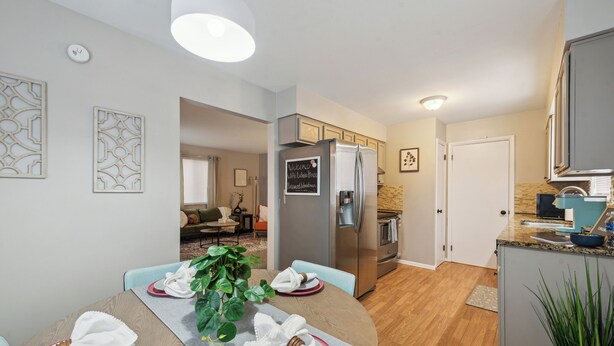 Una cocina moderna con refrigerador empotrado, un comedor con una mesa redonda dispuesta para cuatro personas, y una sala de estar al fondo.