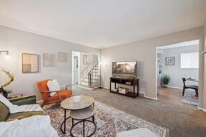 A modern living room with a sofa, armchair, coffee table, and a TV on a stand. A staircase leads to another room. - Spacious & well designed 3br/1.5ba w/ Fiber Wi-Fi! (Toledo)