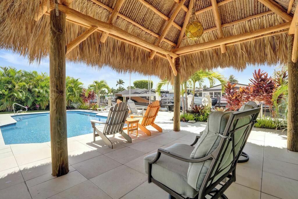 Un espace aménagé au bord de la piscine, doté d’un toit de chaume, de chaises longues et offrant une vue sur la piscine et la végétation tropicale.