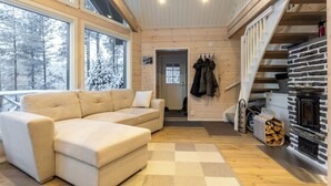 Ein gemütliches Blockhauss-Interieur mit einem beigefarbenen Ecksofa, Holzboden, Kamin und einer Treppe.