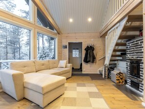 Interior acogedor de una cabaña con un sofá seccional color beige, piso de madera, chimenea y una escalera.