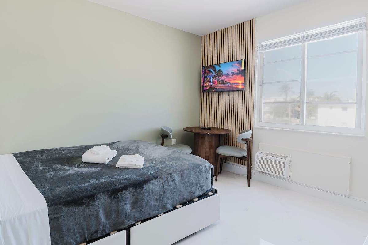 A modern hotel room with a bed, a TV, a small table, and a chair.