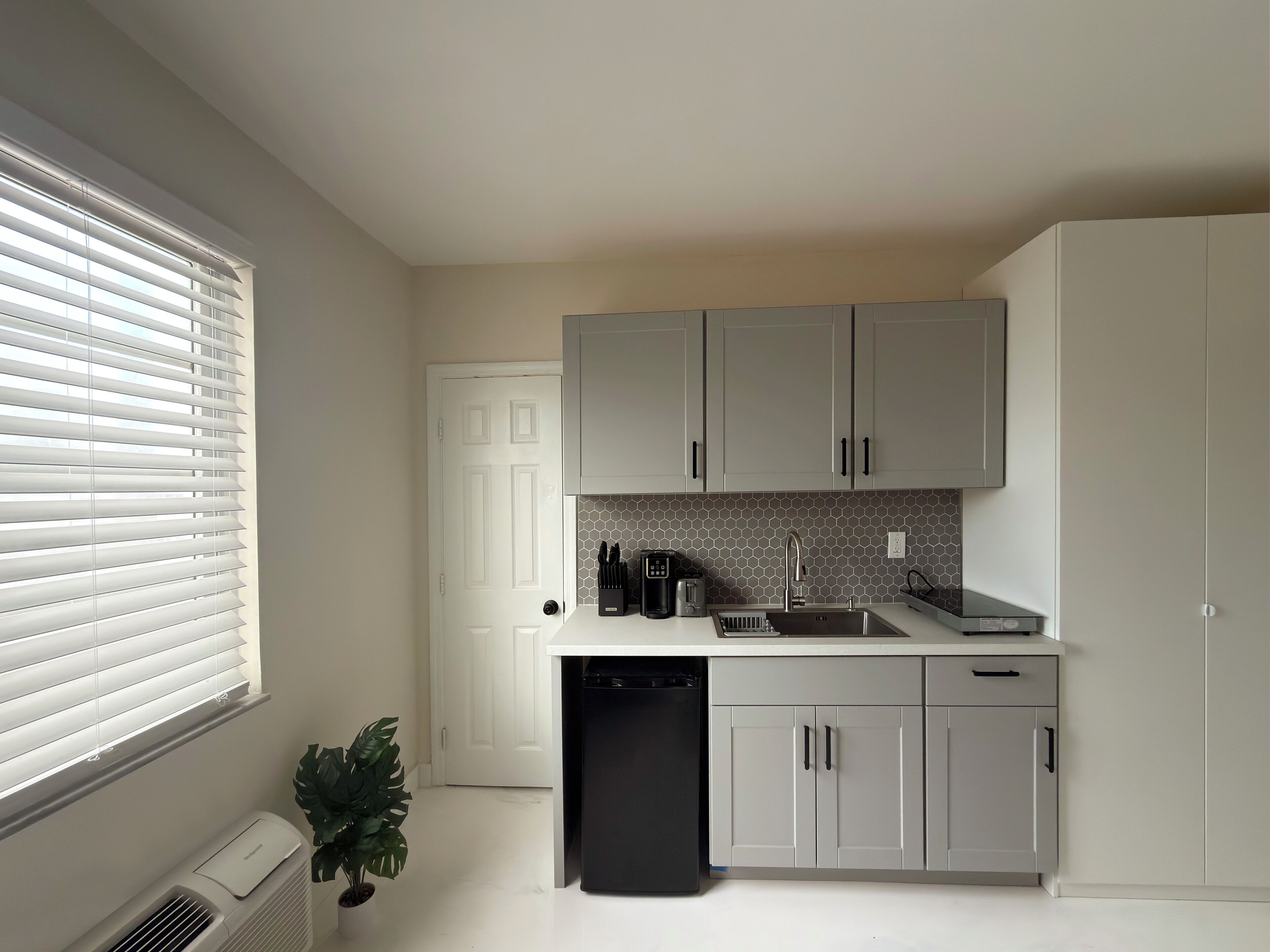 A modern kitchen with grey cabinets, a white countertop, and a black dishwasher.