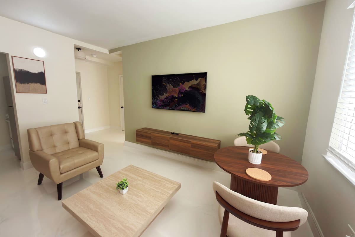 A modern living room with a beige sofa, a coffee table, a round wooden table with a plant, and a large abstract painting on the wall.