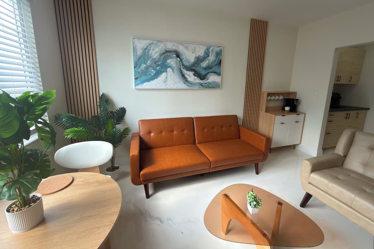 A modern living room with a brown sofa, a white armchair, a glass coffee table, and a painting on the wall.