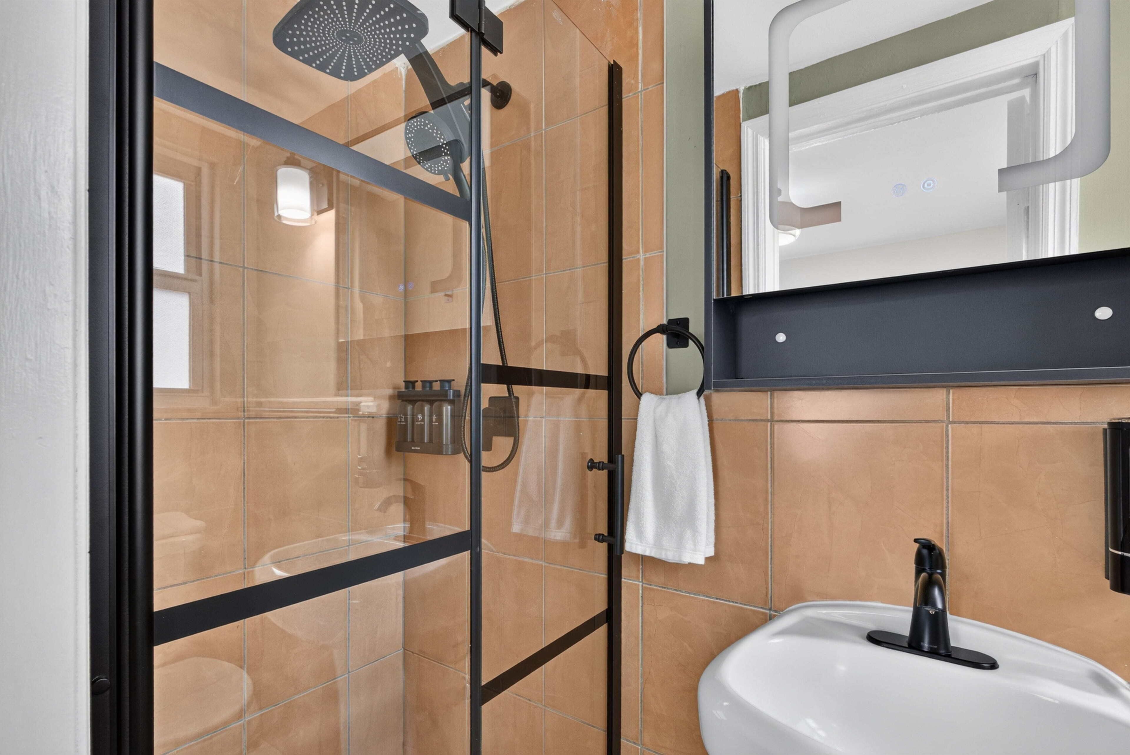 Un baño moderno con cabina de ducha de vidrio, lavamanos blanco y toallero.