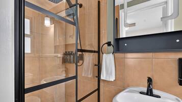 Un baño moderno con cabina de ducha de vidrio, lavamanos blanco y toallero.