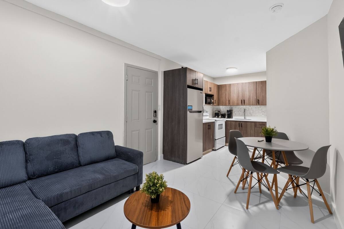 A modern living room with a sofa, a dining table with chairs, and a kitchen in the background.