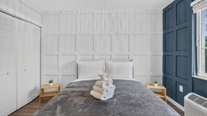 Ein Schlafzimmer mit einem Bett, einem weißen Kopfteil, zwei Nachttischen, einem Fenster und einer Heizung.