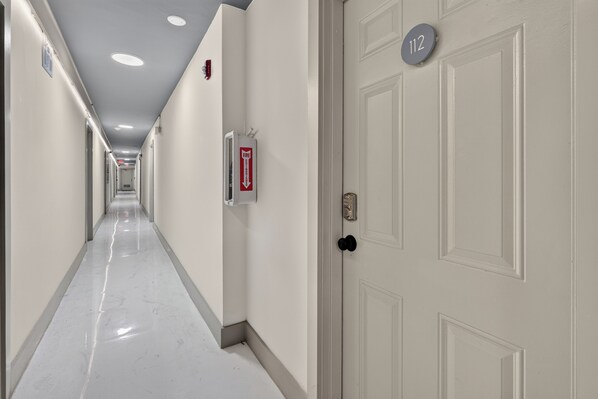 A hotel corridor with white walls, a fire extinguisher, and a door marked with the number 112. - MB Playa Hotel and Apartments (Miami Beach)