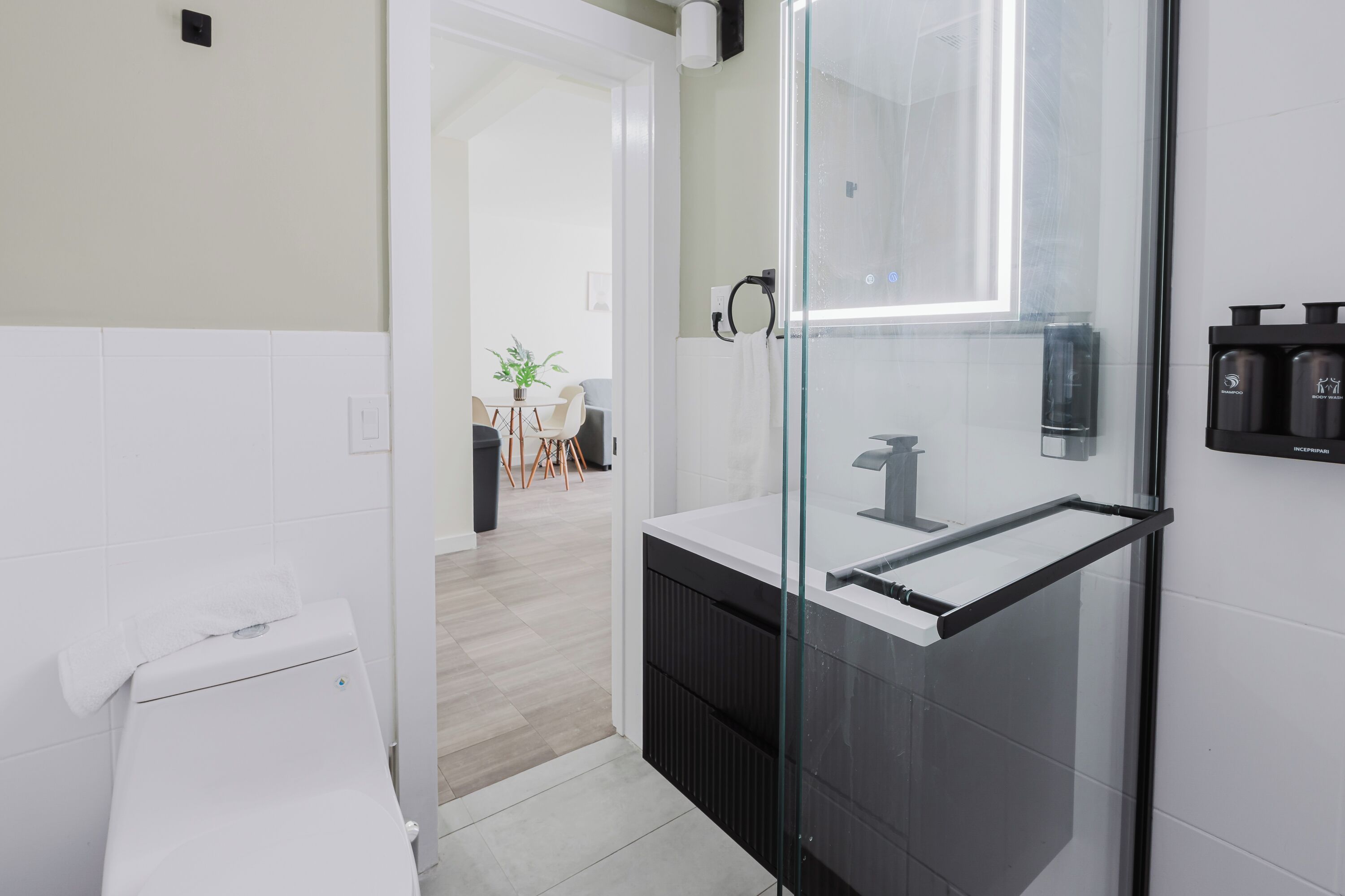 A modern bathroom with a glass shower enclosure, a white sink with a black countertop, and a visible toilet.