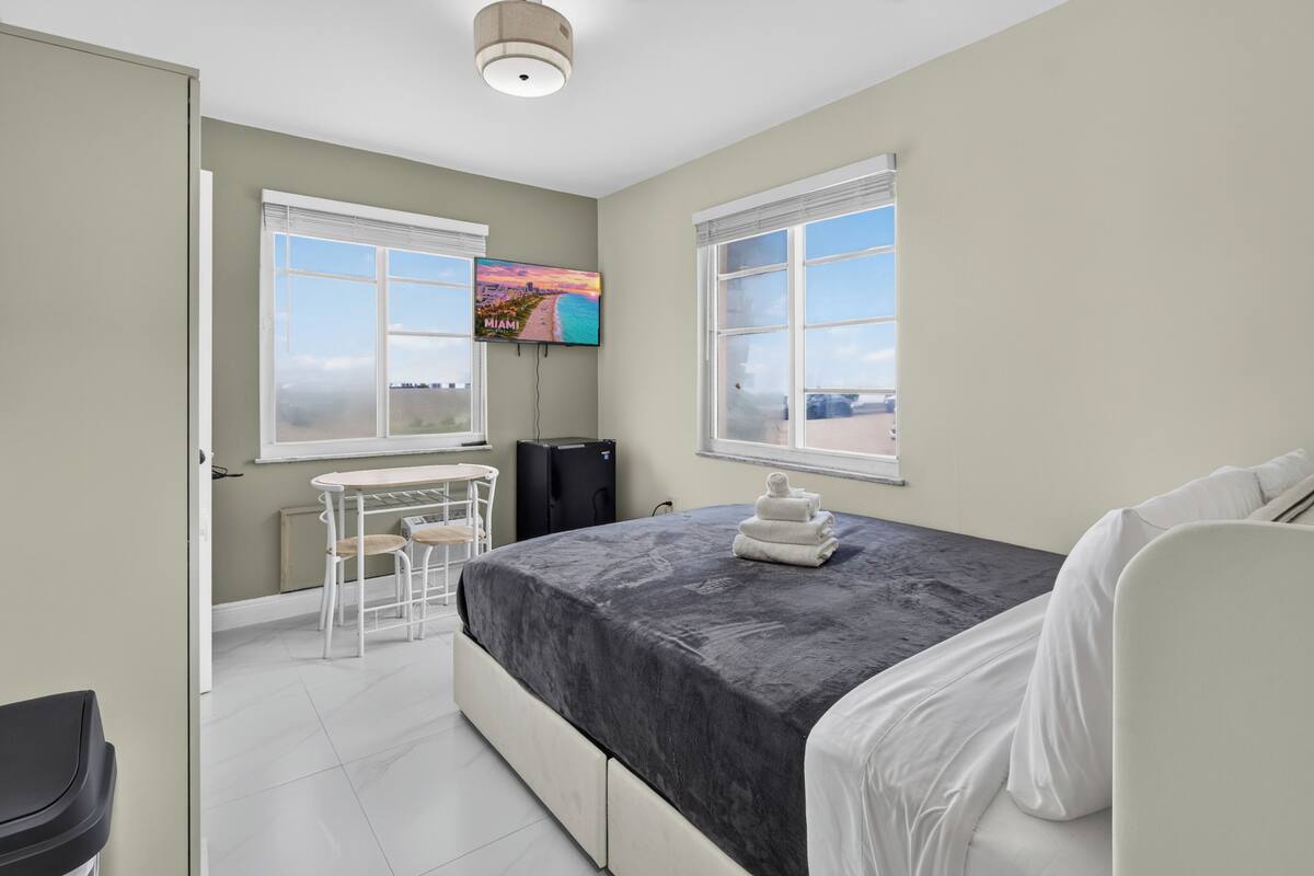 A bedroom with a bed, a desk, a chair, a TV, and a window with a view.