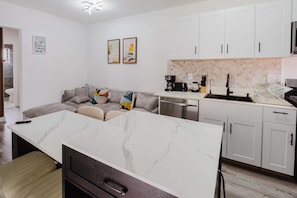 A modern kitchen with white cabinets, a marble island, and a dining area with a sofa.