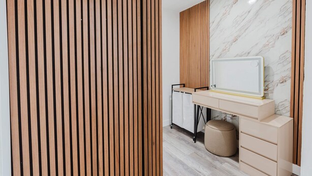 Ein modernes Zimmer mit einer Holzhakepartition, einer Marmorwand, einem Schreibtisch mit Schubladen, einem kleinen runden Hocker und einem Wagen mit einem weißen Schrank.