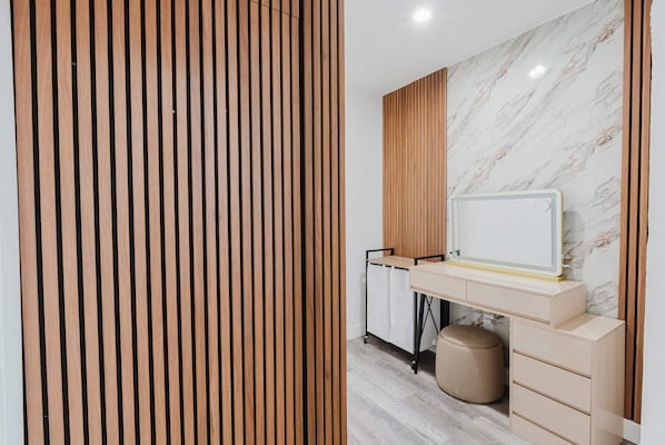 A modern room with a wooden slat partition, a marble wall, a desk with drawers, a small round ottoman, and a cart with a white cabinet.