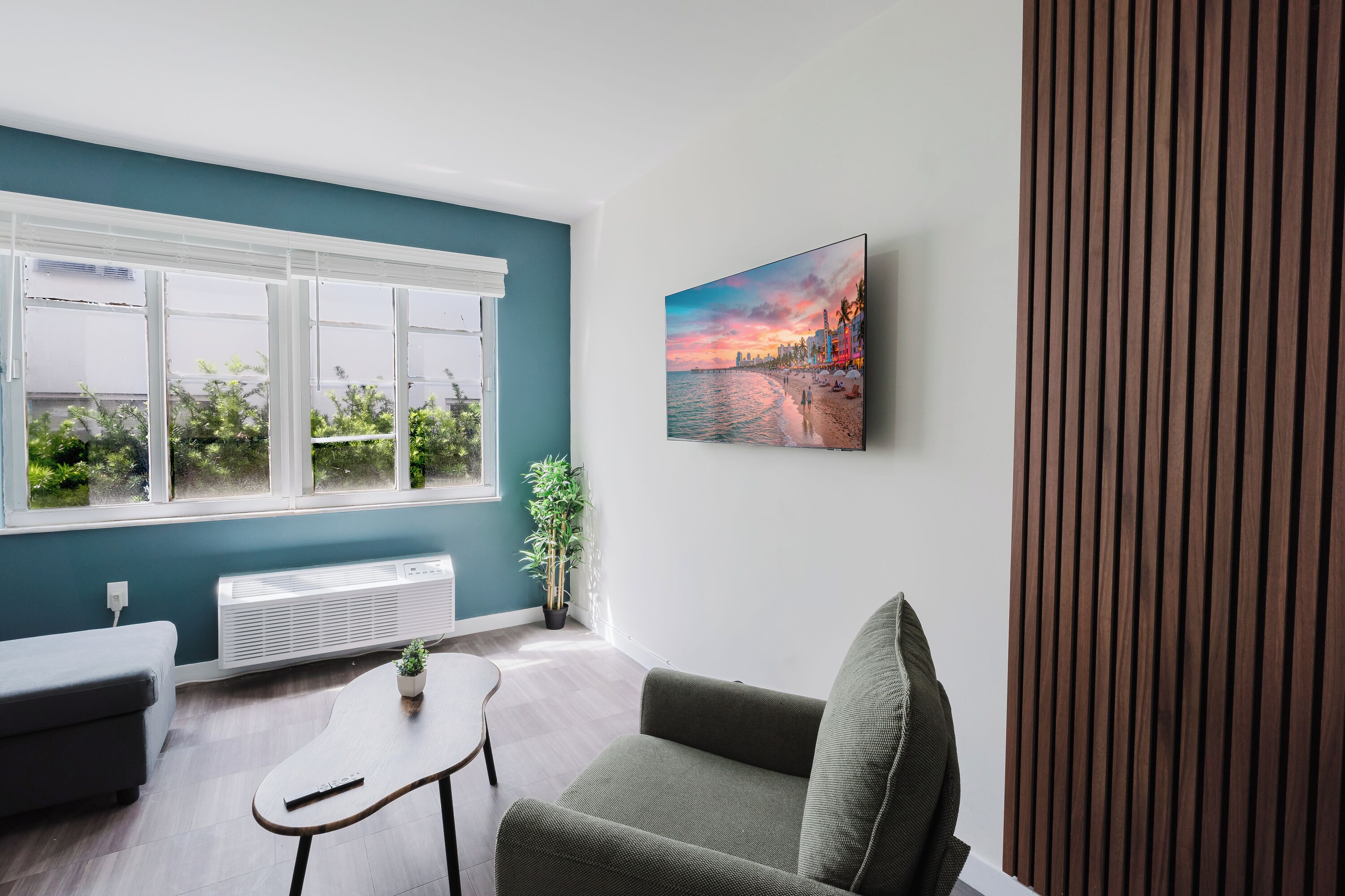 Ein modernes Wohnzimmer mit einem großen Fenster, einem Gemälde, einer Topfpflanze und einer Wandpaneele aus Holz.