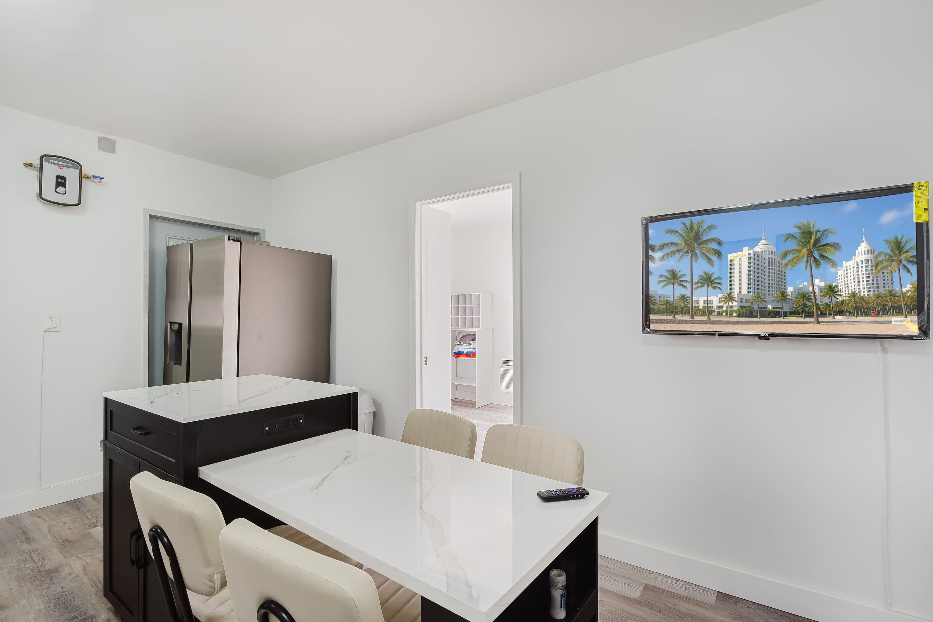A modern kitchen with a built-in refrigerator, a dining area with a marble table, and a TV mounted on the wall displaying a cityscape.