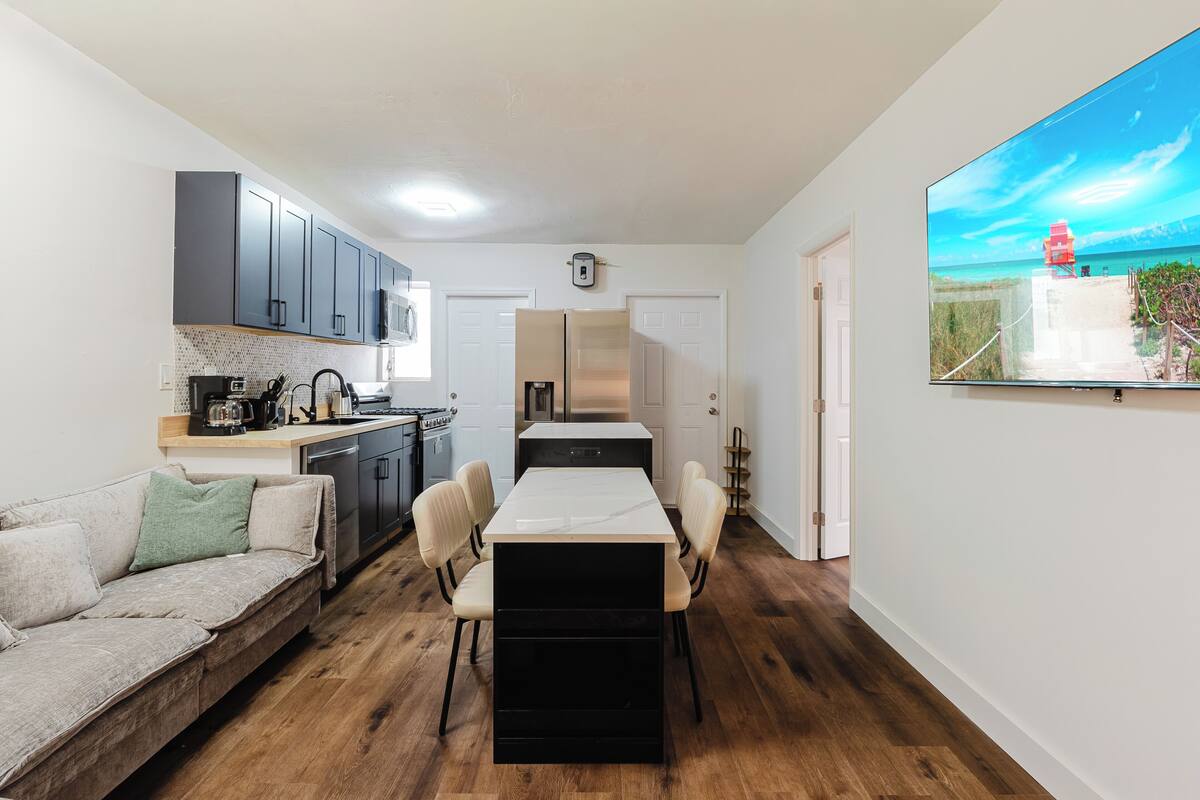 A compact kitchen with modern appliances, a dining area with a central table, and a large window with a beach view.