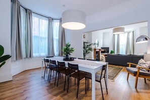 A modern living room with a dining area, large windows, and a fireplace. - 6BDR House | Sleeps 16 | Group Friendly (Manchester)