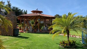A gazebo with a tiled roof, surrounded by a well-maintained lawn and potted plants.