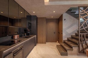 Una cocina moderna con horno empotrado, cafetera y tostadora. Se observa una puerta de madera y una escalera con barandilla geométrica.