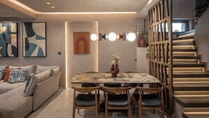 A modern living space with a dining area, a sofa, abstract wall art, and a staircase. - Lapis Nera Villas  (Viannos)