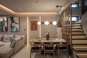 Un espacio habitable moderno con comedor, sofá, arte abstracto en la pared y una escalera.