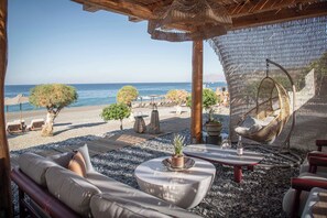 Un salón junto a la playa con asientos exteriores, vista al mar y una estructura de pérgola.