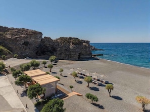 A beachside property with a wooden structure, lounge chairs, and umbrellas. - Lapis Nera Villas (Viannos)