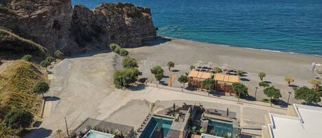 Ein Küstenhotel mit Poolbereich, Strand und einer felsigen Klippe.