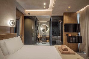 A modern hotel room with a large bed, a bathroom with a vanity, and a television mounted on the wall. - Lapis Nera Villas  (Viannos)