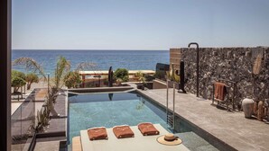 A pool area with clear blue water, a view of the sea, and a stone wall with a sign. - Lapis Nera Villas  (Viannos)