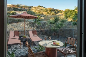 Una terraza con asientos al aire libre, una mesa con un plato de comida y vasos, y vistas a un paisaje montañoso.