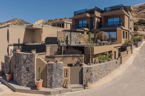 A modern multi-story house with a stone facade, large windows, and a flat roof with outdoor seating. - Lapis Nera Villas  (Viannos)